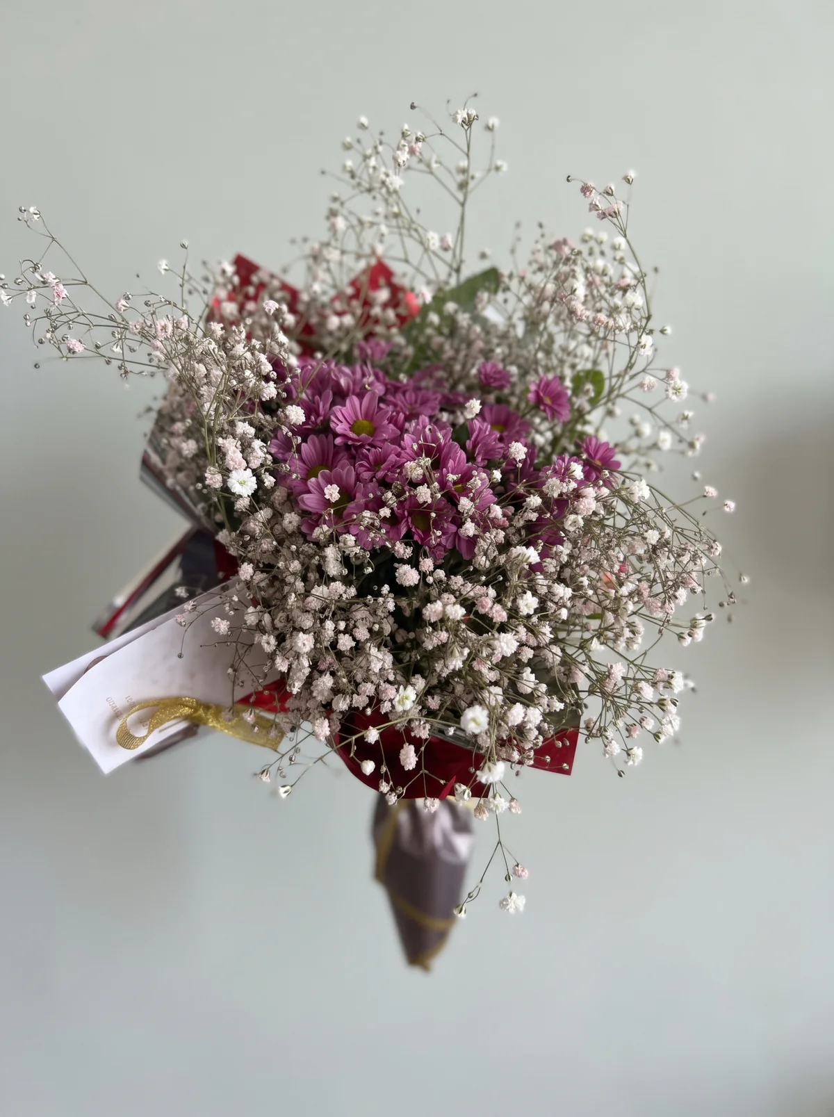 Ramo de flores violetas rodeadas de pequeñas flores blancas y rosadas, con envoltorio rojo y blanco.